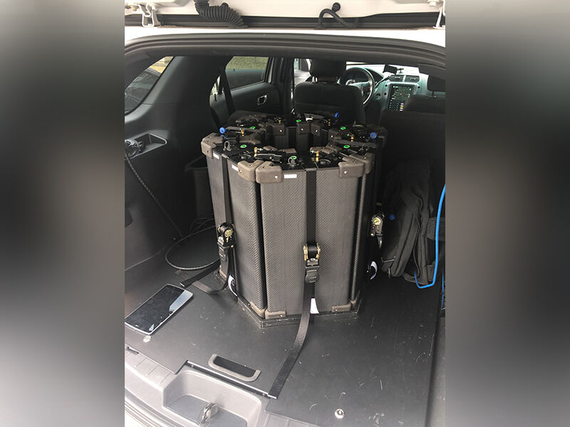 Image looks into the back storage area of a passenger vehicle, which is opened. There are radiation detection sensors, with carbon fiber enclosures, in a hexagonal formation placed in the storage area.